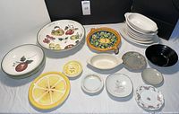 Overview of 14 ceramic dishes including fruit decorated bowls, plates, serving dishes, and teapot arranged on table.
