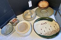 Array of assorted ceramic serving pieces, plates, bowls, and covered pot arranged on white cloth