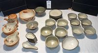 Overall display of various rustic Asian pottery on white cloth - includes teapot, small bowls, spoons, and plates