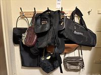 Several purses and bags hanging on wall hooks, showing variety of brands and styles including black quilted, floral, and leather options.