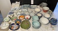 Wide assortment of Asian ceramic dishes and bowls in various colors, patterns, and sizes shown on white surface.