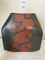 Front view of square jar showing black matte glaze with rust-red geometric patterns