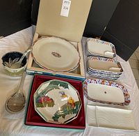 Full lot view showing cake plate in box with tropical bird motif, round Koransha platter in box, rectangular Koransha dishes stacked, sushi dishes, ramen bowl with spoon, and large ceramic spoon with rest.