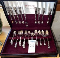 Wide shot of incomplete silverplate flatware set in burgundy felt lined case with white satin cover