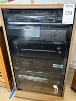 Full view of the stereo components in the wooden cabinet with glass door and caster wheels.
