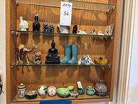 Photo showing three shelves with assorted small decorative figurines and containers including animals, Buddha, boots, and various small dishes and pitchers.