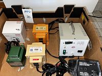 Overview of five step down transformers in various colors and sizes including white, orange, green, yellow, and beige metal enclosures inside a cardboard box.