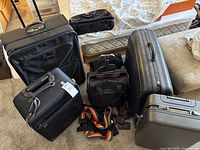Overview of six suitcases and bags on floor and mattress with straps in front