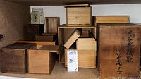 Multiple Japanese wooden storage boxes of various sizes and colors arranged on shelves; some have lids and some do not; one large box has Japanese calligraphy on the front.