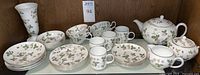 Overview of set arranged on shelf showing plates, bowls, cups, mugs, teapot, sugar bowl, creamer and bud vase