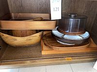 Wide view of wooden serving items on a wooden shelf including salad bowl, platters, covered cake plate, and lazy susan.