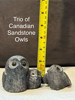 Photo showing three Canadian sandstone owl sculptures with a measuring tape indicating the tallest owl is about 5 inches tall, positioned on a flat surface with a brown background.