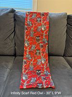 Red infinity scarf featuring owl designs displayed on a dark couch.