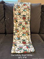 White infinity scarf with vibrant owl print displayed on a dark couch, showing full length and pattern details.