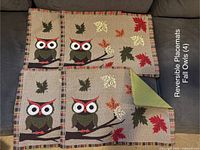 Photo showing four reversible cloth placemats with embroidered fall owl and leaf designs on a beige background with multicolored stripe border, one placemat flipped to show solid olive green reverse side.