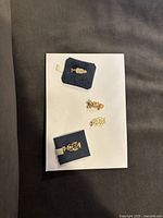 Top-down view of four gold owl charms placed on white paper with two on black velvet holders, showing varied owl designs including one with star accent.