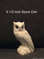 Front view of the white stone owl carving with notable green glass eyes and detailed feather carving.