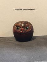 Photo of a closed wooden owl trinket box featuring carved owl face with detailed feathers and black eyes. The box is about 2 inches tall.