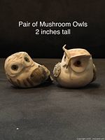 Front facing view of two carved mushroom owl figurines, approximately 2 inches tall, showing detail in carving and eyes.