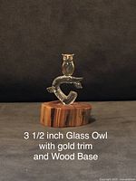 Glass owl figurine with gold trim on wood base shown against a dark background.