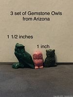 Photo showing three owl figurines carved from gemstones, two smaller (pink and dark green) and one larger green owl, all standing against a background with text noting size and origin.