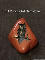 Close-up photo of a triangular polished red-orange gemstone with a carved owl silhouette inset in black or dark stone.