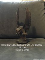 Owl figurine carved from wood, wings raised, placed on cushion background, shows repair to one wing.