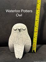 Front view of a white ceramic owl figurine with crackle glaze next to yellow measuring tape showing approximately 5.5 inches height