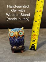 Front-facing image showing the hand-painted owl figurine on its wooden stand with a measuring tape indicating approximate height of 2.5 inches.