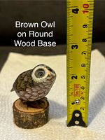 Brown carved owl figurine on round wood base with tape measure showing height approx 2.5 inches.