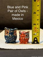 Photo showing blue and pink owl figurines with a measuring tape indicating their height, confirming size and hand painted details.