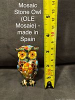 Front view of colorful mosaic stone owl figurine with yellow measuring tape showing height at approximately 3.5 inches, black background