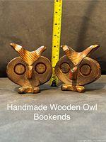 Front view of two carved wooden owl bookends, featuring detailed feather carvings and natural wood stain with a measuring tape indicating height near 6 inches.