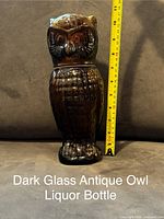 Front view of the dark glass owl-shaped liquor bottle showing its height of approximately 10.5 inches alongside a measuring tape.