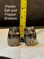 Two pewter owl salt and pepper shakers side by side with a tape measure showing about 2.5 inches in height