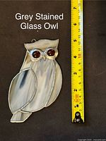 Grey stained glass owl with orange eyes approx 5 inches tall next to measuring tape