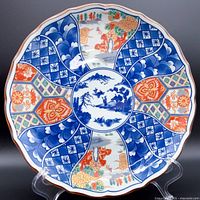 Front view of plate showing central blue scenic landscape with surrounding geometric and floral patterns in blue, orange and gold color palette.