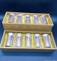 Set of 10 copper tumblers wrapped in plastic inside two gold-colored boxes lined with yellow fabric.
