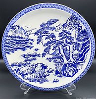 Front view of a 12-inch blue and white porcelain plate with detailed landscape design including mountains, trees, houses, boat, and water with a patterned rim.