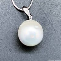 Front view of the rounded genuine pearl pendant on the silver chain, showing its pearly white color with some surface marks.