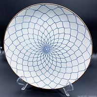 Front view of the white porcelain sashimi plate showing detailed blue fishnet geometric pattern with a brown rim on a plate stand.