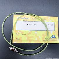 Full view of the 19-inch natural peridot beaded necklace arranged on a black surface with a gem grading report card beneath it, confirming natural peridot stones.