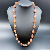 Front view of 27 inch natural orange stone necklace with wired cage chain on a black necklace stand.