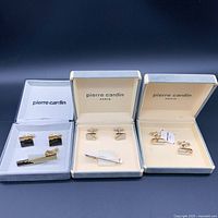 Three open Pierre Cardin branded boxes each containing cufflinks and a tie clip set.