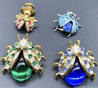 Four ladybug pin brooches shown together on a black background, featuring gold-tone and blue metal designs with rhinestones and glass stones.