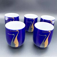 Front and angled view of all five cobalt blue porcelain teacups with gold and grey crane design on exterior