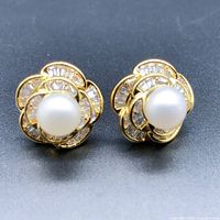 Front view of the pair of flower design earrings with pearls and crystals on gold-plated metal.