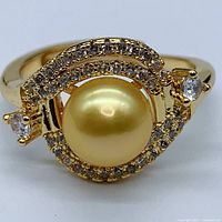 Close-up front view of the adjustable ring showcasing the golden pearl center and surrounding small clear cubic zirconia stones with two larger cz stones on the sides.