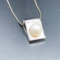 Close-up view of the front of the silver-tone rectangular pendant with round cultured pearl, hanging on silver-tone box chain.