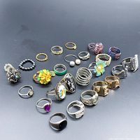 Photo of assorted silver and gold tone rings showing various designs including floral, gemstone, beaded, and patterned styles.